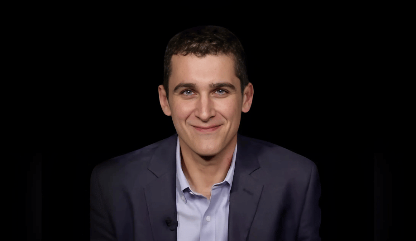 Richard is a white man of Semitic appearance in his late 30s. He smiles and wears a blue s